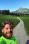 The picture shows a sporty employee in front of a mountain panorama