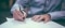 The image shows two hands in close up signing a paper.
